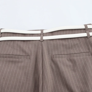 Close-up of brown pinstripe trousers featuring stylish double white waist belts