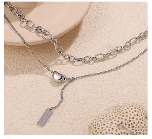 Detail of silver double-layer stainless steel necklace with bean pendant and metal tag