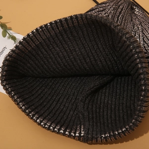 Macro detail of thick knit texture and metallic silver finish on a black beanie