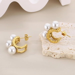Detailed view of C-shaped 18k gold plated earrings with shell pearls on textured stone