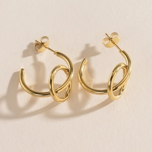 Macro shot of gold-plated stainless steel twisted hoop earrings on beige background