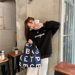 Street style view of a blue canvas tote bag paired with a black sweatshirt and white pants