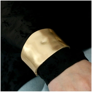 Close-up of wide matte gold cuff bracelet featuring an irregular geometric textured design