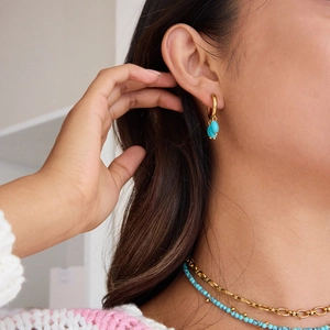 Close-up of 18k gold earrings featuring turquoise pendants on a model with matching jewelry