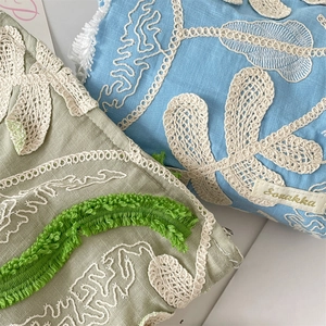 Detailed macro view of 3D embroidered floral lace and Suzakka logo on cosmetic bags