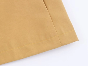Detail of double-needle stitching and twill texture on a mustard yellow short trench coat
