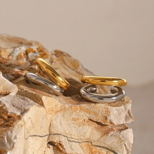 Macro shot of gold and silver minimalist smooth wide-band steel earrings on textured stone