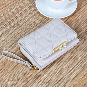 Short pink quilted faux leather wallet for women with pearl clasp and wrist strap on wood