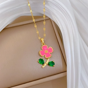 Détail du collier fleur dorée avec pétales roses et feuilles vertes sur ruban blanc