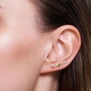 Close-up of a gold ear crawler with multi-colored zircon stones worn on an ear