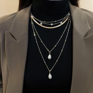 Detail of multilayer gold necklace with water drop pearls on a dark blazer and turtleneck