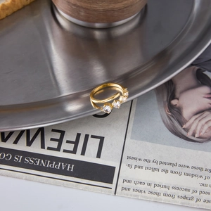 Golden titanium steel open ring with four clear zircons displayed on a metal plate