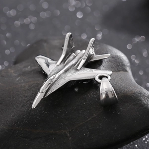 Close-up of a silver titanium steel fighter jet pendant on a textured dark stone background