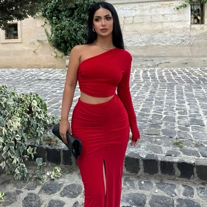 Detail of red one-shoulder crop top and high-waisted side slit skirt set in outdoor setting