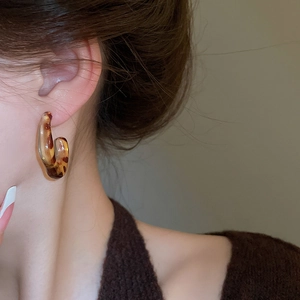 Close-up of leopard pattern C-shaped resin earrings on model's ear for vintage style
