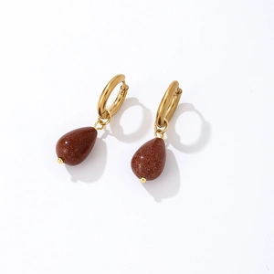 Macro detail of gold hoop earrings with brown teardrop goldstone charms on white background