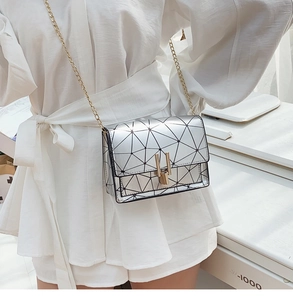 Detail of silver geometric crossbody bag with gold chain strap on white outfit