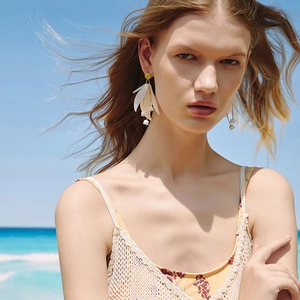 Close-up of elegant white floral drop earrings worn by a model against a beach backdrop