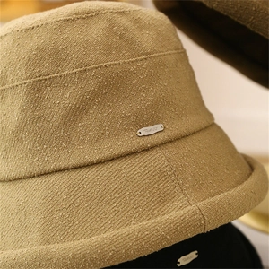 Dettaglio del cappello pescatore kaki con trama in tessuto grezzo e placca logo argento