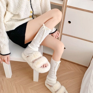 Detail of white cable knit leg warmers with delicate bows and plush faux fur slippers
