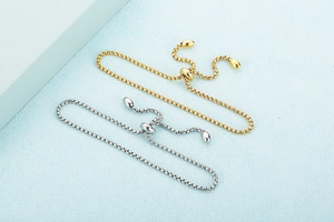 Detail of adjustable gold and silver box chains with sliding clasps on a textured surface