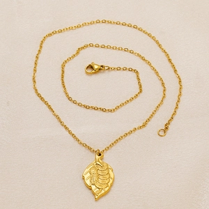 Minimalist titanium steel leaf pendant necklace with fine gold-plated chain on beige surface