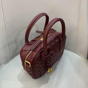 Close-up of wine red woven textured mini handbag with gold zipper and knotted handle detail
