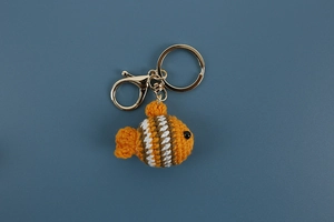 Detailed close-up of handmade crochet clownfish keychain with vibrant stripes and gold metal clasp