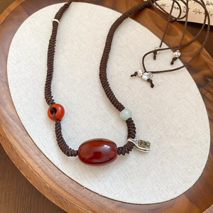 Detailed macro view of woven wax cord necklace with large oval red agate and retro metal charm
