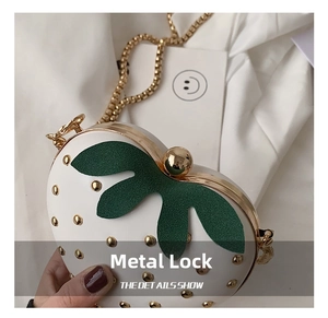 Close-up of golden strawberry clasp and green leaf hardware on white chain bag