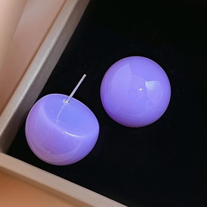 Detailed close-up of glossy purple acrylic ball earring on black velvet display