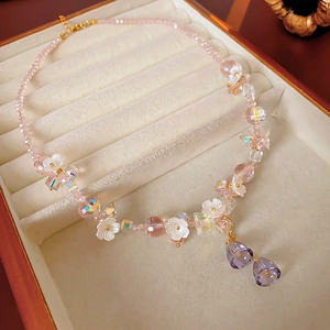 Close-up of pink crystal beaded necklace with small white flowers and purple bell pendants