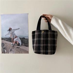 Close-up of retro plaid tweed handbag featuring black fabric handles and golden snap button