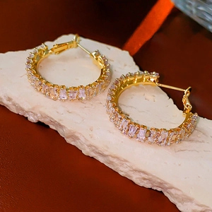 Close-up of gold hoop earrings with baguette-cut zircons on a textured stone stand