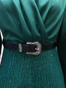 Close-up of a black faux leather belt with a silver vintage engraved buckle on a model