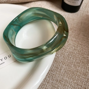 Close-up of translucent green resin bangle with marble texture on a white plate