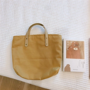 Detail of yellow canvas tote bag with white leather handles and gold rivet fasteners