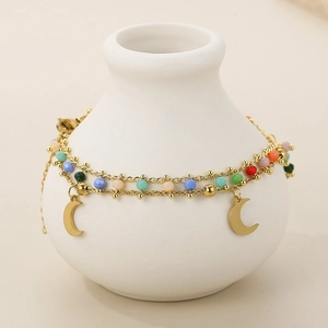 Detail of double-layered gold bracelet with colorful beads and moon charms on a ceramic vase