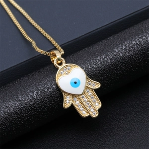 Macro shot of gold Hamsa hand pendant with crystal pavé and blue heart evil eye detail