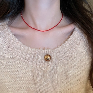 Close-up of a faceted red crystal beaded necklace worn on a beige knitted sweater