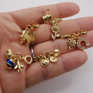 Gold charms collection with travel and floral themes for bracelets shown on hand