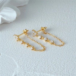 Macro detail of S925 silver gold-plated flower chain earrings with sparkling zircons