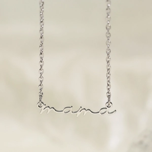 Gros plan du pendentif Mama en argent poli sur une chaîne fine et tissu beige doux