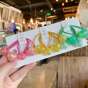 Close-up of glitter-filled gradient heart and round ball hair ties in pink, yellow, and green