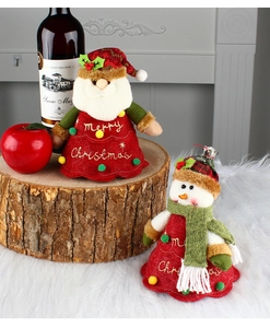 Detail of plush Santa and Snowman bottle covers on a cozy wooden and fur surface