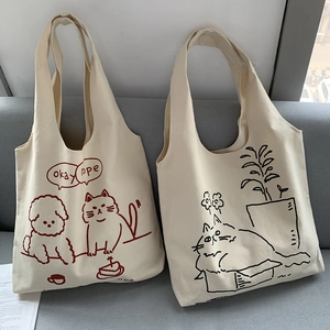 Detail of cream canvas tote bags with cute cat illustrations on a gray sofa