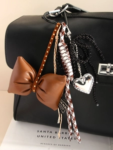 Detail of brown leather bow and braided rope charm with silver heart on a black bag