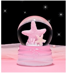 Close-up of pink ocean crystal ball with starfish decor on a textured base