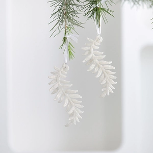 Glittery white acrylic fern leaf Christmas ornaments hanging on a pine branch