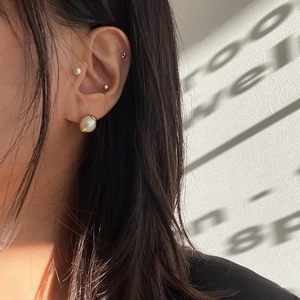 Detailed view of pearl earrings and multiple gold stud piercings on a female ear